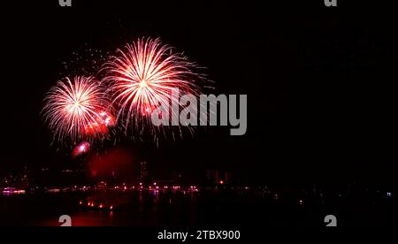 Atemberaubendes scharlachrote Feuerwerk mit Gefälle, das am Nachthimmel über dem Hafen plätschert Stockfoto