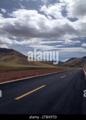 Ein malerisches Bild einer Autobahn, die durch die Wüste führt, mit majestätischen Bergen im Hintergrund und wunderschönen weißen Wolken Stockfoto