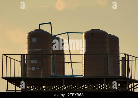 Cremefarbener Kunststoff-Wassertank für den Außenbereich auf dem Turm. Der Kunststoff-Wassertank ist hoch installiert, um das Wasser abzusenken. Wassertank vor dem Haus. Stockfoto