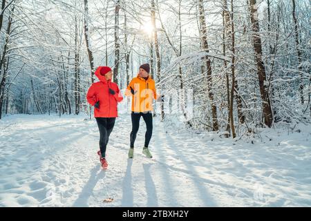 Lächelnde Läuferinnen und Läufer mittleren Alters trugen helle winddichte Jacken und liefen während der sonnigen Eiszeit im malerischen, schneebedeckten Wald Stockfoto