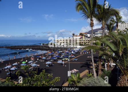 Der vulkanische schwarze Sandstrand in La Arena auf Teneriffa, den Kanarischen Inseln, voller Urlauber. Stockfoto