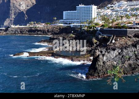 Blick auf das Dorf Los Gigantes auf Teneriffa und die dramatische Küste mit einem natürlichen Pool, der vom Meer und den vulkanischen Klippen hinter dem Resort gebildet wird. Stockfoto