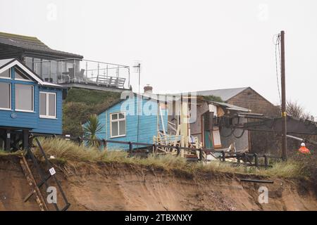 Abrissarbeiter reißen das zweite von fünf Häusern auf den Klippen des Dorfes Hemsby ab, das von der Küstenerosion betroffen ist. Hohe Fluten und starke Winde führten letzten Monat zum Zusammenbruch einer privaten Zufahrtsstraße in Hemsby in Norfolk. Bilddatum: Samstag, 9. Dezember 2023. Stockfoto
