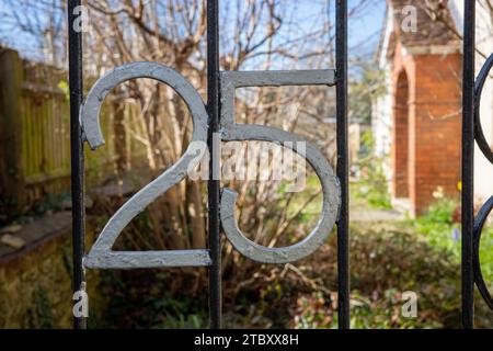 Nummer 25 auf einem schmiedeeisernen Tor mit Garten dahinter. Stockfoto