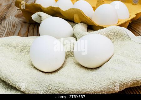 Frische weiße Eier auf hellem Hintergrund. Frische Hühnereier liegen auf einem gelben Handtuch auf dem Küchentisch und in einem Tablett. Stockfoto