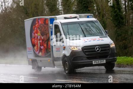 Milton Keynes, Bucks, UK - 9. Dezember 2023: 2021 Mercedes Benz Sprinter Transporter für Tesco-Heimlieferungen auf nasser Straße, im Regen mit Kopflicht Stockfoto