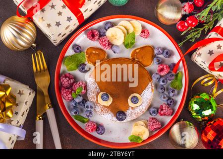 Lustige und süße Weihnachts-kleine Fuchspfannkuchen auf einem rot weißen Teller dekoriert mit frischer Beere, Obst und Puderzucker, Kinderweihnachtfrühstück Stockfoto