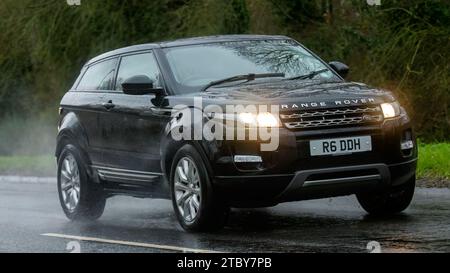 Milton Keynes, Bucks, Großbritannien - 9. Dezember 2023: 2014 Dieselmotor Range Rover Evoque Auto fährt auf nasser Straße, im Regen und bei eingeschalteten Scheinwerfern Stockfoto