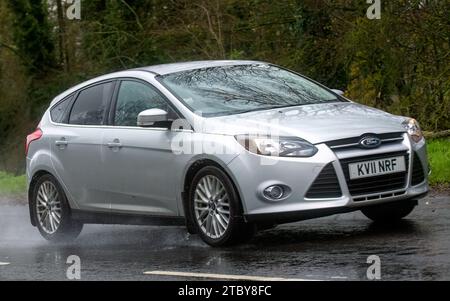 Milton Keynes, Bucks, UK - 9. Dezember 2023: 2011 silbernes Ford Focus Auto fährt auf nasser Straße, im Regen mit Scheinwerfern Stockfoto