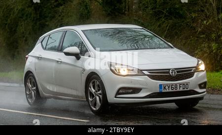 Milton Keynes, Bucks, UK - 9. Dezember 2023: 2018 weißes Vauxhall Astra Auto, das auf nasser Straße fährt, im Regen mit Scheinwerfern an Stockfoto