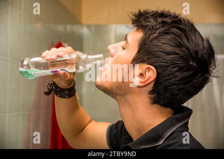 Kopf und Schultern Nahaufnahme des attraktiven jungen Mannes mit dunklem Haar Spülen mit Mundwäsche im Badezimmer als Teil der Morning Grooming Routine Stockfoto