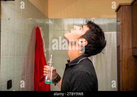 Kopf und Schultern Nahaufnahme des attraktiven jungen Mannes mit dunklem Haar Spülen mit Mundwäsche im Badezimmer als Teil der Morning Grooming Routine Stockfoto