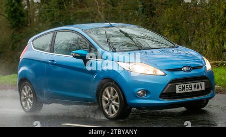 Milton Keynes, Bucks, UK - 9. Dezember 2023: 2009 blaues Ford Fiesta Auto fährt auf nasser Straße, im Regen mit Scheinwerfern an Stockfoto