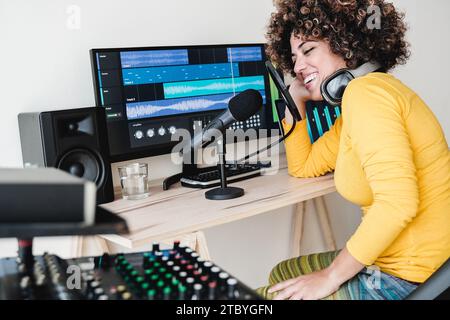 Weibliche Latin-Host-Podcast-Aufnahme am Computer mit Kopfhörern und Mikrofon. Frau streamt Live-Radio im Studio Stockfoto