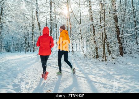 Lächelnde Läuferinnen und Läufer mittleren Alters trugen helle winddichte Jacken und liefen während der sonnigen Eiszeit im malerischen, schneebedeckten Wald Stockfoto