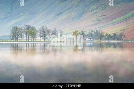 Der berühmte Blick über Buttermere auf die berühmte Char Hut am Südufer, mit der nebeligen Herbstlandschaft, die sich im ruhigen Wasser spiegelt. Stockfoto