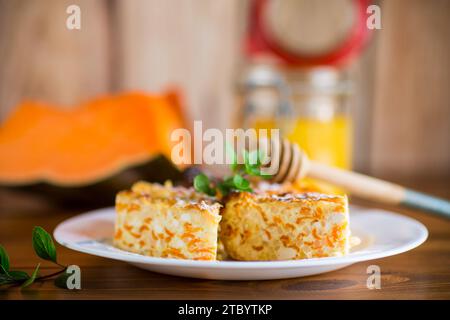 Gekochter Hüttenkäse-Auflauf mit Kürbisstücken im Inneren, auf einem Holztisch. Stockfoto