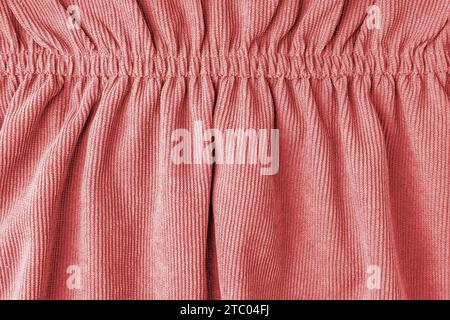 Rotes Cordmaterial mit elastischer Nahaufnahme. Samtstruktur mit Falten und Vorhängen. Stoffoberfläche, Textilinhalt, Tapete, Hintergrund. Stockfoto