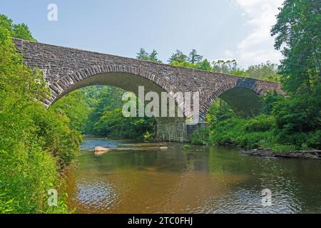 Die Linville River Stone Arch Bridge über einen ruhigen Fluss in North Carolina Stockfoto