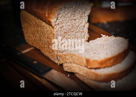Braunes Brot auf dem Schneidebrett, das geschnitten wird Stockfoto