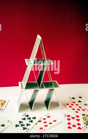 Spielkartenpyramide im Gleichgewicht, mit Pokerkarten auf rotem Hintergrund und verstreuten Karten Stockfoto