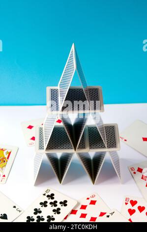 Spielkartenpyramide im Gleichgewicht, mit Pokerkarten auf blauem Hintergrund und verstreuten Karten. Stockfoto
