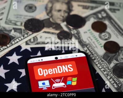In dieser Fotoabbildung wird ein OpenDNS-Teil des Cisco-Logos auf einem Smartphone mit US-Dollar-Banknoten und -Münzen im Hintergrund angezeigt. Stockfoto
