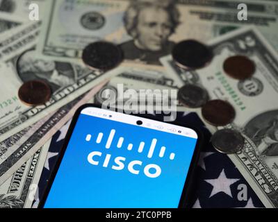 In dieser Fotoabbildung wird das Cisco Systems Logo auf einem Smartphone mit US-Dollar-Banknoten und -Münzen im Hintergrund angezeigt. Stockfoto