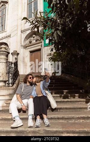 Romantisches verliebtes Paar, das Treppen auf der Altstadtstraße sitzt und Selfie am Telefon macht Stockfoto