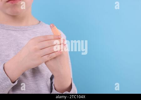 Kleiner Junge, der Pflaster auf den Finger vor hellblauem Hintergrund klebt, Nahaufnahme. Leerzeichen für Text Stockfoto