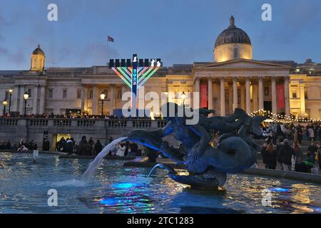 London, Großbritannien. Dezember 2023. Die riesige Menora auf dem Trafalgar-Platz am dritten Tag von Chanukah wird von der Polizei beobachtet, während ein pro-palästinensischer Protest in der Nähe stattfindet. Zehntausende marschieren von der City of London zum Parlamentsplatz und rufen zu einem dauerhaften Waffenstillstand im Gazastreifen auf, während der Krieg zwischen Israel und der Hamas eine zweimonatige Grenze überschreitet. Quelle: Eleventh Photography/Alamy Live News Stockfoto