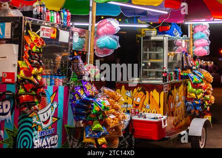 Bunte Snackkarren am Abend mit Zuckerwatte, Chips, rasiertem Eis und Limonaden Stockfoto