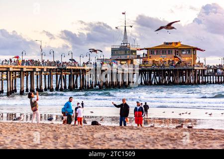 Touristen machen Fotos am Santa Monica Beach, mit Santa Monica Pier im Hintergrund, Sommernachmittag in Südkalifornien Stockfoto