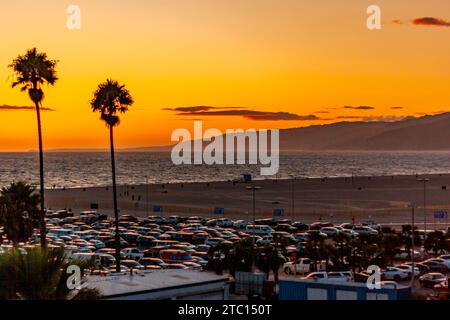 Sonnenuntergang am Santa Monica Beach mit Palmen in Silhouette, Santa Monica, Kalifornien, mit Autos, die im Sommer am Strand in Südkalifornien geparkt werden Stockfoto