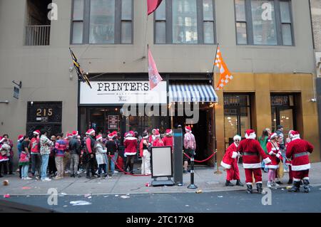 New York, Usa. Dezember 2023. SantaCon-Teilnehmer in Weihnachtsmannskostümen und anderen Weihnachtsoutfits warten online, um eine Bar zu betreten. In Manhattan, New York City, versammelten sich Schwärmer, die als Weihnachtsmann verkleidet waren, zur SantaCon, einem jährlichen Weihnachtsbummel, der Geld für wohltätige Zwecke sammelte. Die Spender erhielten Zutritt zu teilnehmenden Veranstaltungsorten wie Bars und Clubs. (Foto: Jimin Kim/SOPA Images/SIPA USA) Credit: SIPA USA/Alamy Live News Stockfoto