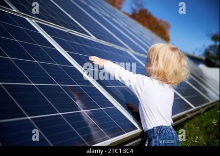 Neugieriger Junge, der daran interessiert ist, wie Sonnenkollektor funktioniert. Ein kleines Kind, das sich die dunkelblaue Solarbatterie ansieht. Das Konzept der jungen Generation und der alternativen Energie. Stockfoto