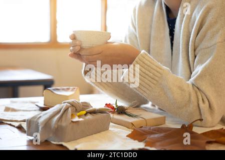 Eine Frau, die eine Teetasse hält, umweltfreundliche Geschenkverpackung auf dem Tisch.Out FOCUS Stockfoto