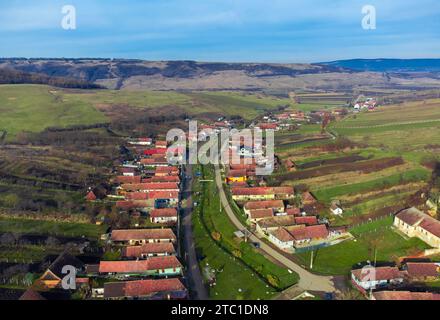 Ein Blick aus der Vogelperspektive auf ein malerisches Dorf in Rumänien, umgeben von üppigen grünen Hügeln. Stockfoto