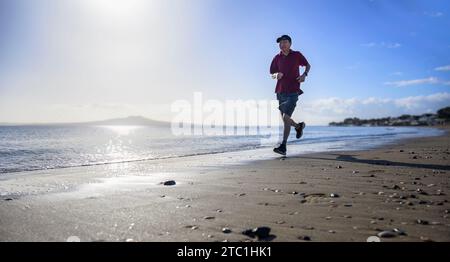 Mann, der am Morgen am Strand läuft. Vorderansicht. Milford Beach. Auckland. Stockfoto
