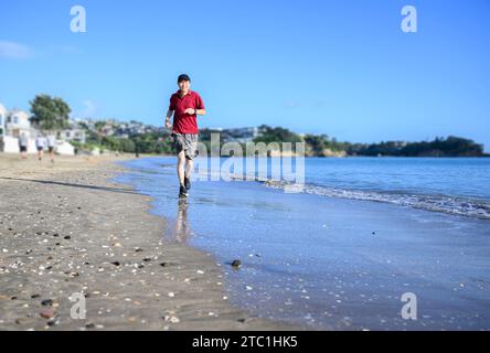 Mann, der am Strand läuft, mit Reflexion auf dem nassen Sand. Milford Beach. Auckland. Stockfoto