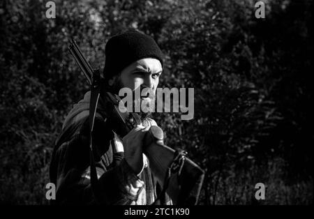 Bärtiger Jäger mit Waffe und Spaziergang im Wald. Jäger mit Schrotflinte auf der Jagd. Stockfoto