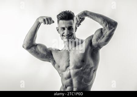 Ein Bodybuilder-Mann, der seine Muskeln auf einem Schwarzweißfoto im Studio spannt und die Kamera lächelnd ansieht Stockfoto
