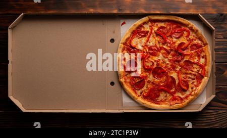 Paprika-Pizza mit Paprika in offener Kartonbox auf dunklem Holztisch flach liegend mit Kopierraum Stockfoto
