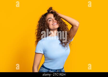 Fröhliche Frau mit Hand im Haar auf gelbem Hintergrund Stockfoto