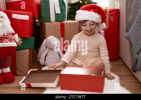 Ein entzückendes Mädchen, das zu Hause am weihnachtsbaum sitzt Stockfoto