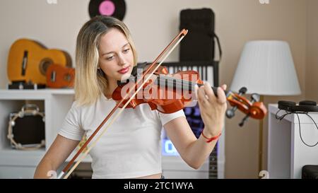 Junge blonde Musikerin, die im Musikstudio Violine spielt Stockfoto