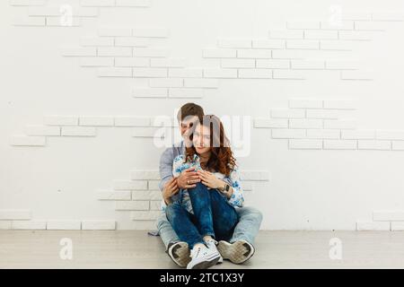 Ein traumhaftes Paar, das auf dem Boden liegt, in einem leeren Raum liegt und aufblickt. Stellen Sie sich ein zukünftiges Innenraumprojekt vor, weißer Hintergrund. Stockfoto