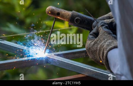 SMAW-Schweißen von quadratischen Metallstahlrohren mit grünem Hintergrund auf modernste Weise Stockfoto