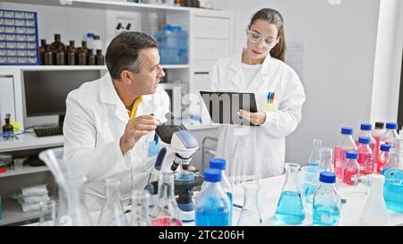 Wissenschaftler arbeiten im Labor zusammen, konzentrieren sich ernsthaft auf ihre Forschung, schreiben auf Zwischenablage, verwenden Mikroskop Stockfoto