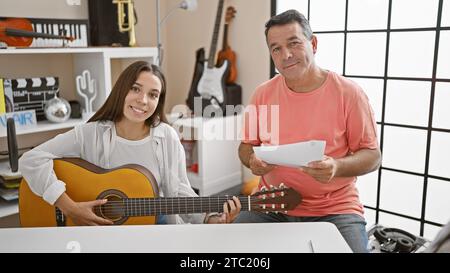 Lächelnde männliche und weibliche Musiker, die in einem klassischen Gitarrenunterricht in einem gemütlichen Musikstudio ihre Liebe zur Musik teilen. Stockfoto